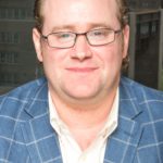 A man wearing glasses and a blue jacket.