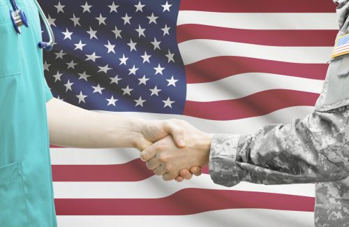 Two soldiers shaking hands in front of an american flag.
