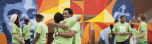 A group of people hugging in front of a colorful mural.